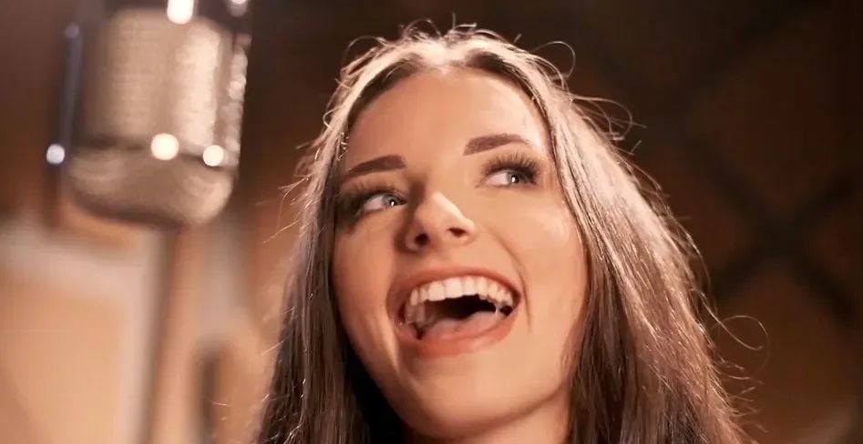 Close-up of Klara Jazbec mid-song at a vintage condenser microphone, eyes lifted, warm amber studio light