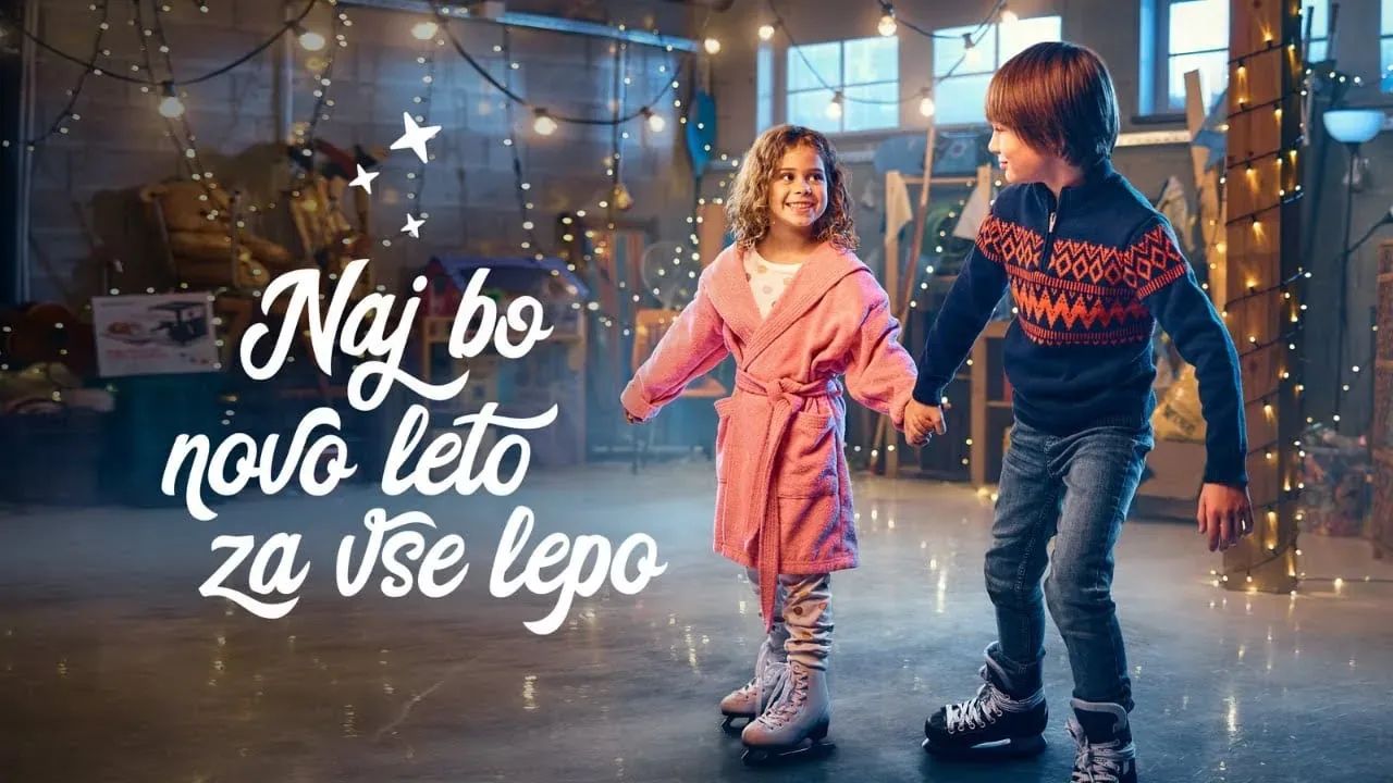 Two children — a girl in a pink robe and a boy in a Nordic-pattern knit sweater — ice-skating hand in hand inside a string-lit warehouse, beside the Slovenian campaign tagline "Naj bo novo leto za vse lepo"